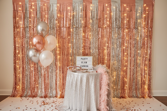 Elegant rose gold and silver tinsel curtain backdrop creating a glamorous DIY photo booth setup with party decorations and soft lighting, demonstrating affordable party decor ideas