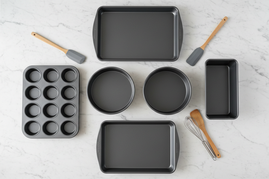 Essential non-stick bakeware collection for beginners including cookie sheets, cake pans, muffin tin, loaf pan, and baking pans arranged on marble countertop
